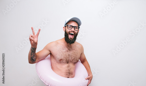 Portrait of a cheerful young hipster man shirtless with pink inflatable ring. Summer vacation, white background. Crazy emotions.