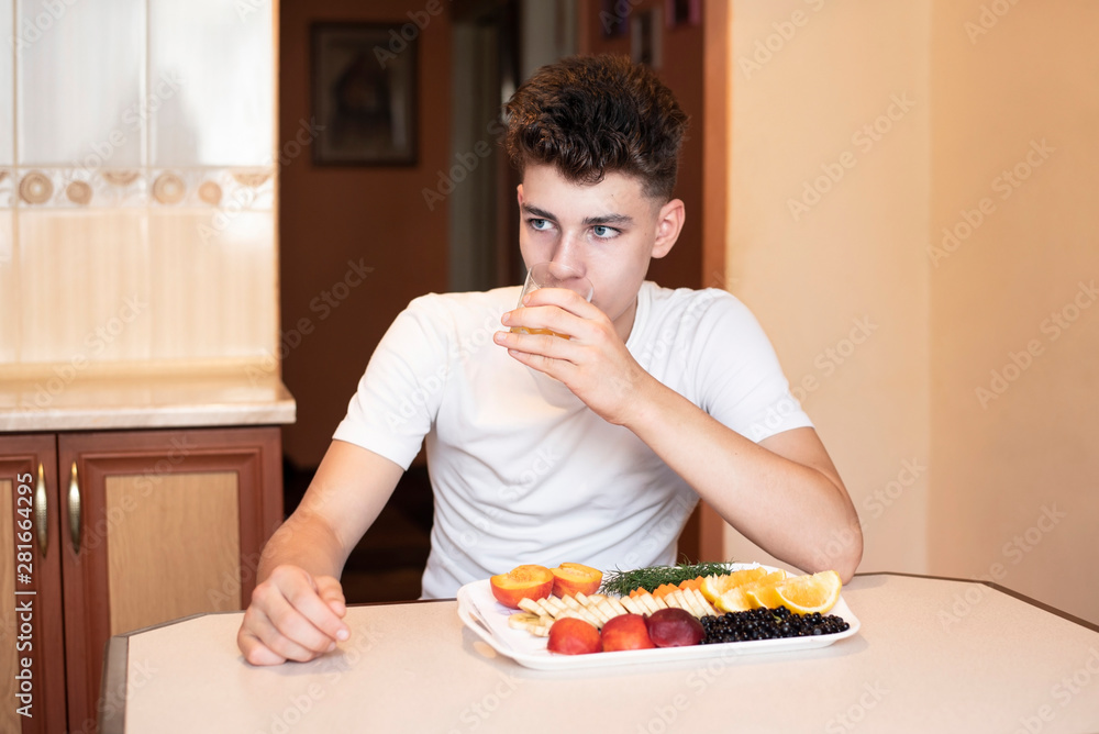 Handsome young man sporting bodybuilding sitting at table drinking orange juice and eating fruit Handsome young man sporting bodybuilding sitting at table drinking orange juice and eating fruit