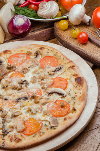 Italian pizza with chicken, tomatoes, mushrooms and cheese on a wooden board, the background is wooden decorated with vegetables and cutlery