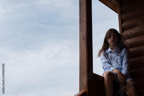 sad girl sitting on the stairs against the sky. girl in dark shadow.