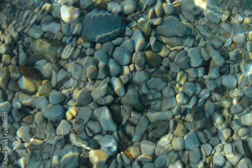 Beautiful colorful pebbles and big stone under turquoise blue clear water, scenic marine background or texture, top view