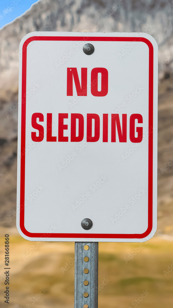 Vertical frame Close up of a No Sledding sign with a towering mountain in the background Vertical frame Close up of a No Sledding sign with a towering mountain in the background