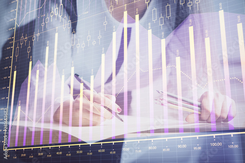 Double exposure of hands making notes with forex chart huds. Stock market concept.