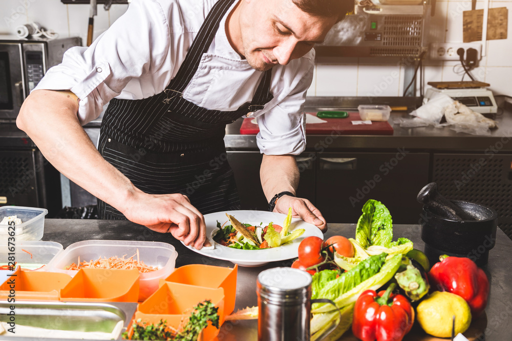 Professional chef cooking in the kitchen restaurant at the hotel, preparing dinner. A cook in an apron makes a salad of vegetables and pizza. Professional chef cooking in the kitchen restaurant at the hotel, preparing dinner. A cook in an apron makes a salad of vegetables and pizza.