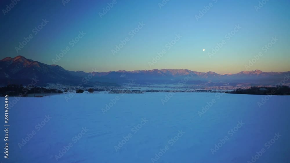 Snowy field and mountains at sunrise with full moon Snowy field and mountains at sunrise with full moon