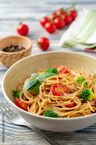 Whole wheat spaghetti pasta with broccoli  cherry tomatoes and basil in bowl on wooden background. Selective focus.