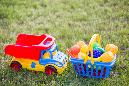 Car truckand a basket with toy fruit and vegetables. Bright plastic colorful toys for children outdoors on sunny summer day. photo