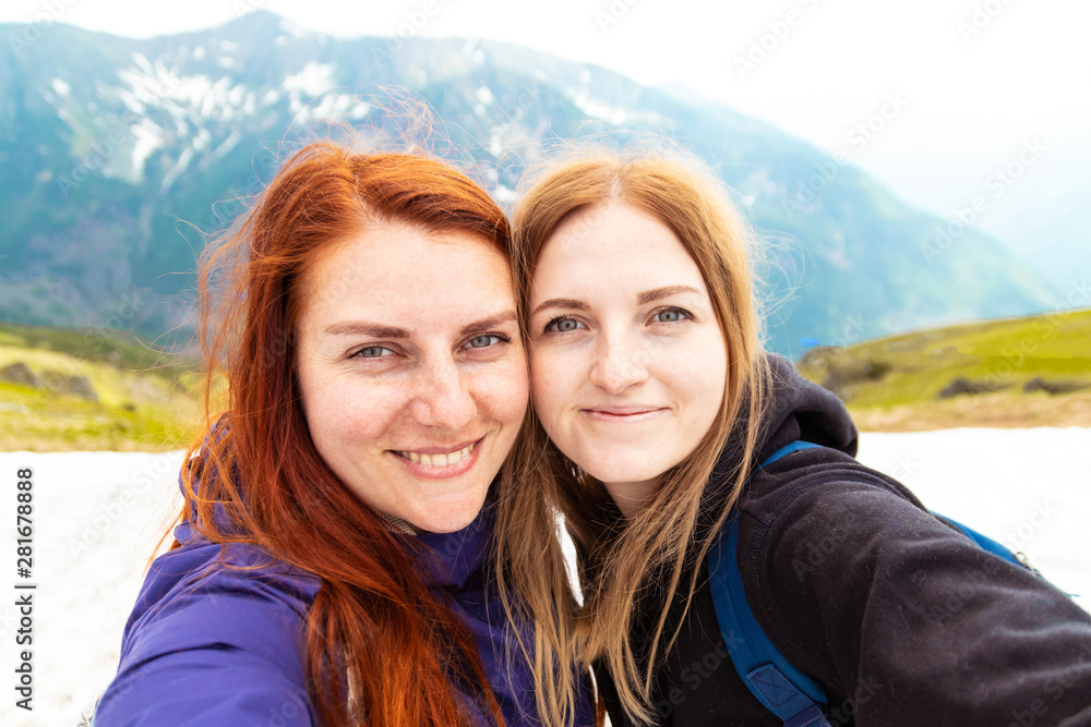 Two girls take a picture with their mobile. Two friends enjoy nature and the outdoors.