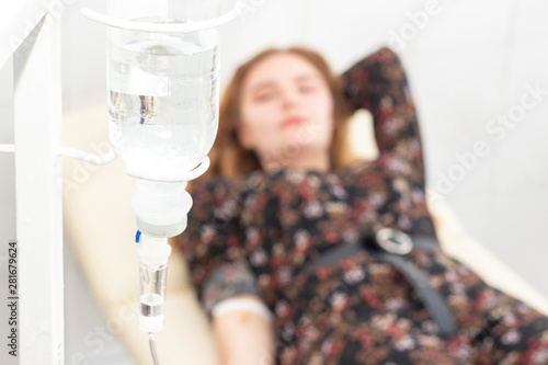 Closeup of saline drip with background Woman patient on the bed get better, when they come for treatment in room hospital. concept healthcare and medicine photo