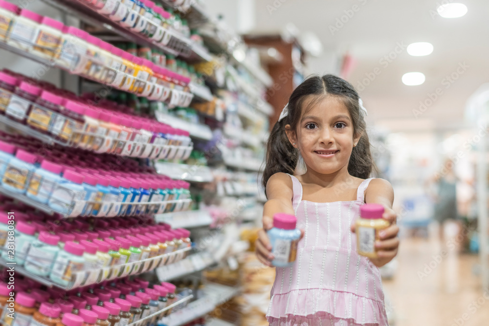 Little girl with paint bottles in supermarket looking at camera