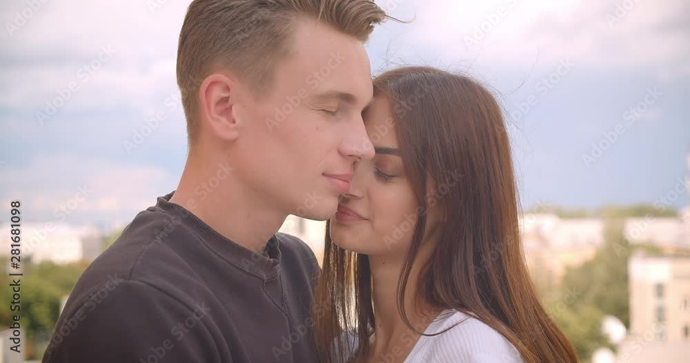 Closeup portrait of young cute caucasian couple hugging standing on the balcony of their house with beautiful landscape on the background Closeup portrait of young cute caucasian couple hugging standing on the balcony of their house with beautiful landscape on the background