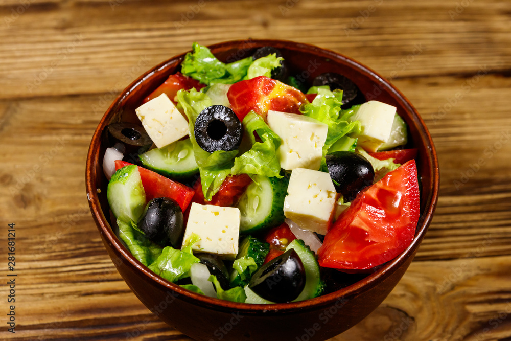 Greek salad with fresh vegetables, feta cheese and black olives on wooden table Greek salad with fresh vegetables, feta cheese and black olives on wooden table