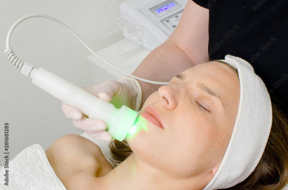 Naklejka premium beautician doing green led light therapy to female customer in beauty salon, facial photo therapy for skin pore cleansing. Anti-aging treatments and photo rejuvenation procedure