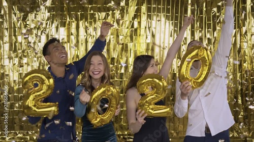 2020 year. falling golden confetti .4 people with golden letters made of foil are dancing on a gold background. 4K photo