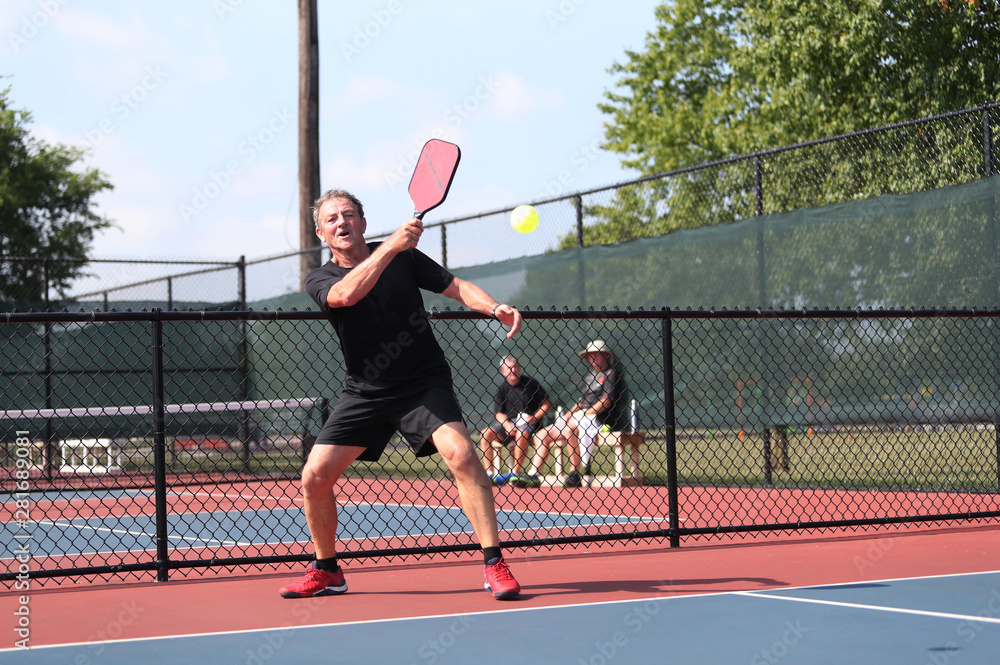 A senior athlete hits a shot, competing in singles, of a pickleball tournament.