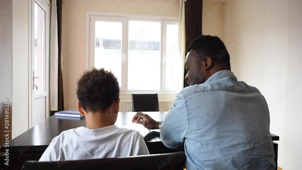Father and son do homework at home. Tutor teaches the boy at home. Home schooling. African american teacher and mixed boy. Father and son do homework at home. Tutor teaches the boy at home. Home schooling. African american teacher and mixed boy.