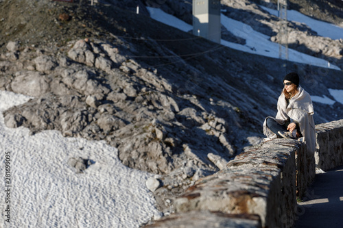 The girl sits on a background of mountains. Against the background of snowy mountains in a hat and sunglasses.