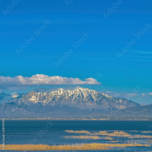 Vivid blue sky with puffy clouds over a snow peaked mountain and calm lake