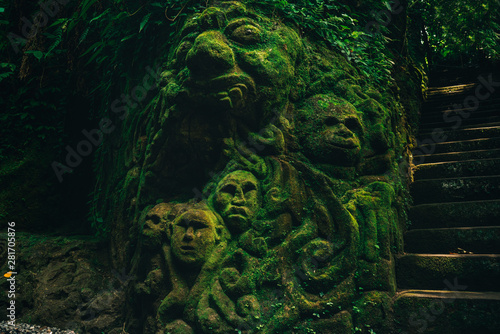 Carving demons faces on wall background covered with moss texture in Bali