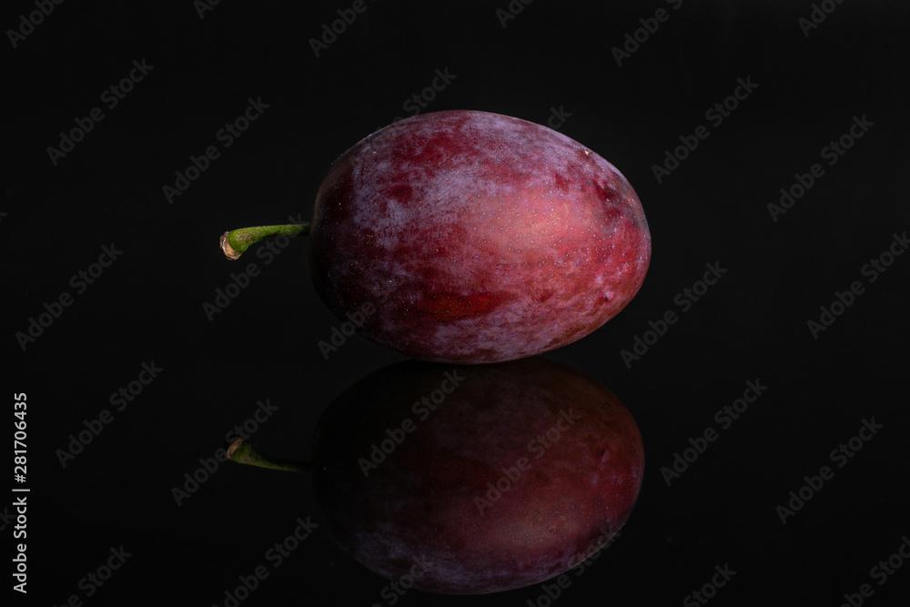 One whole fresh blue plum isolated on black glass One whole fresh blue plum isolated on black glass