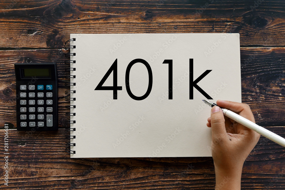 Top view of calculator,notebook and hand holding pen writing 401k. Top view of calculator,notebook and hand holding pen writing 401k.