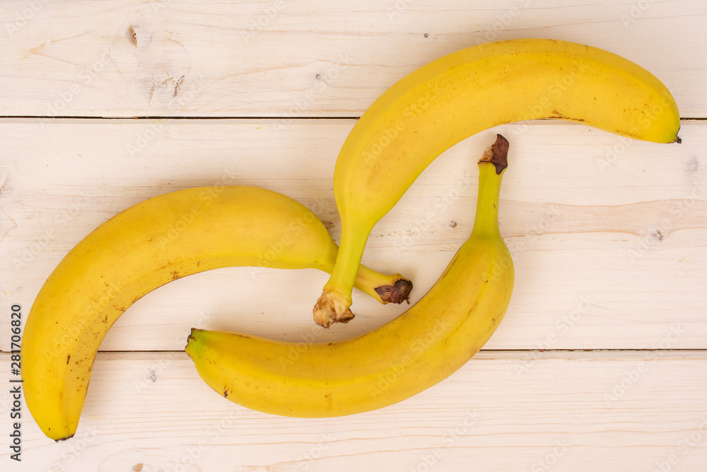 Group of three whole ripe yellow banana placed diagonally flatlay on white wood Group of three whole ripe yellow banana placed diagonally flatlay on white wood