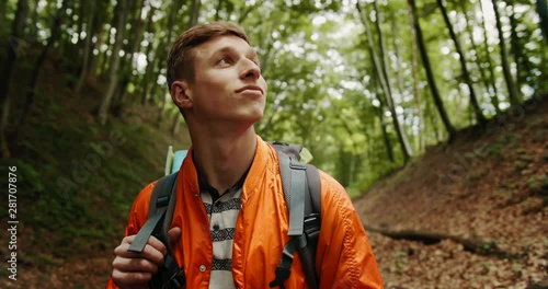 Young handsome male tourist with backpack standing in forest and looking around, eco-tourism