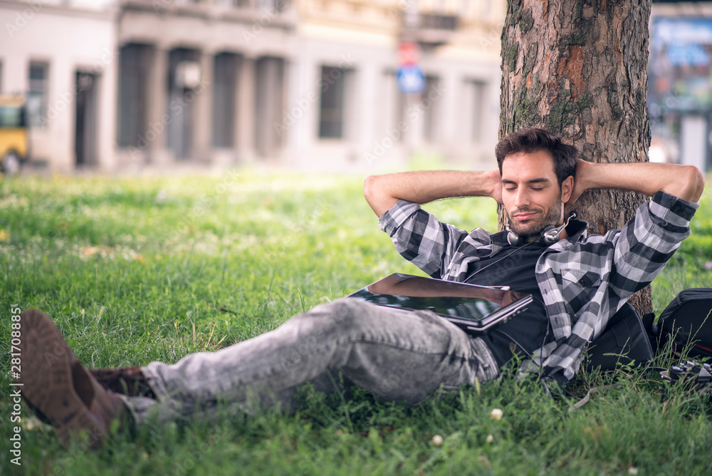 Young urban guy relaxing on the grass, leaning against tree Young urban guy relaxing on the grass, leaning against tree