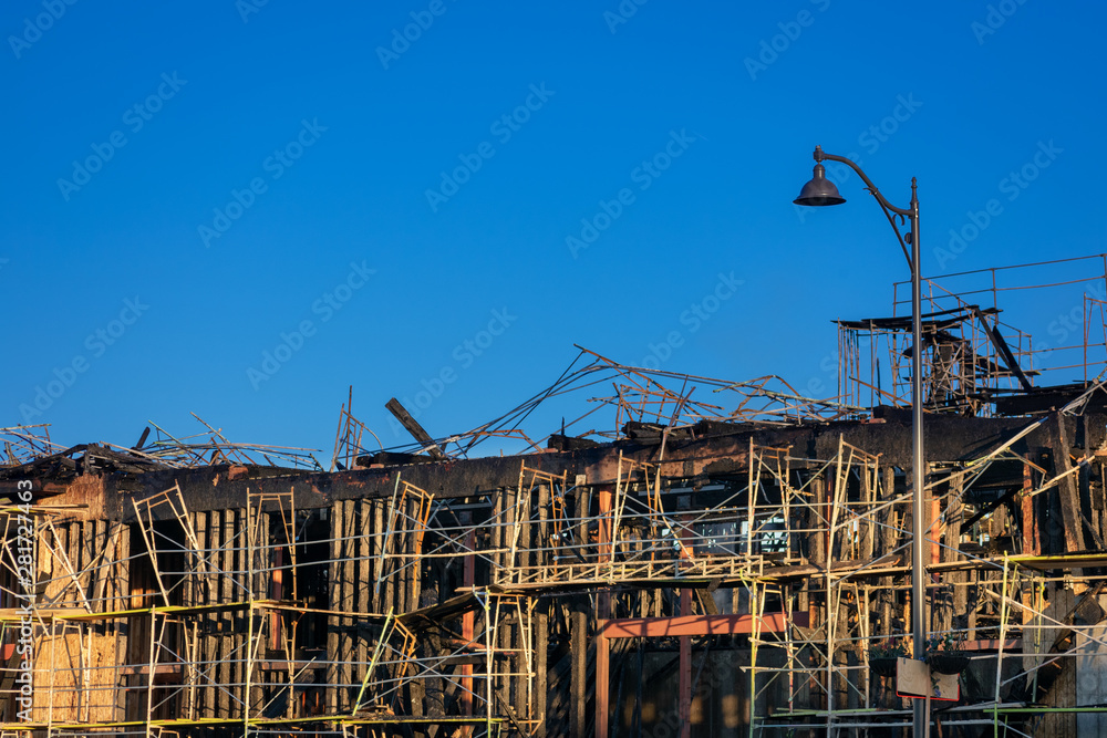 Burned down wooden residential apartment, house, or condo complex exterior after construction site fire. Charred frame and walls, burnt roof and construction scaffolding