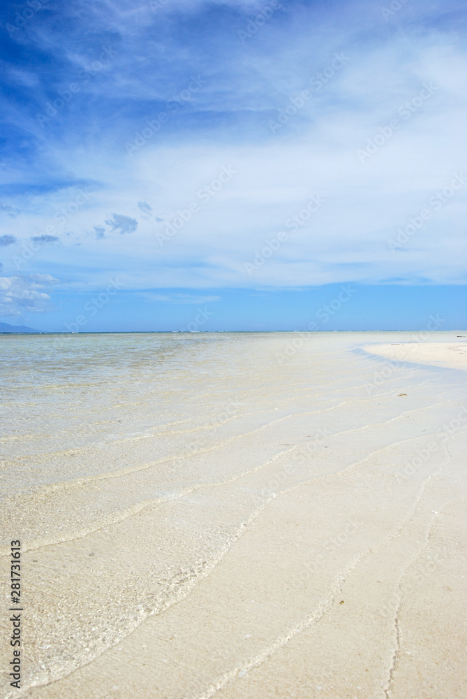 Soft waves of clear water on a clean sandy beach. Above the horizon, an intense blue sky with some clouds - Philippines, Asia.            
