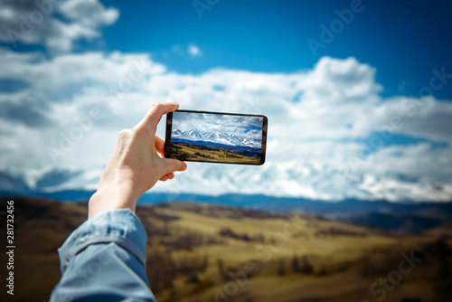 Close-up of female hand holding smartphone and taking photo or video. Woman traveler on the background of a snowy mountain range takes photos on a mobile phone. The concept of travel.