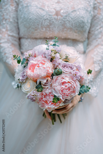 Stylish bride in a white dress holds an unusual wedding bouquet close-up. Delicate wedding bouquet of different flowers in the hands of the bride  selective focus.