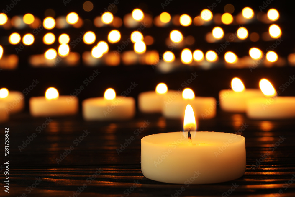 Burning candle on black table against blurred background, space for text Burning candle on black table against blurred background, space for text