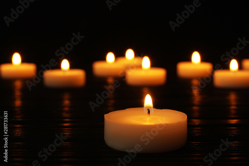 Burning candle on black table against blurred background, space for text