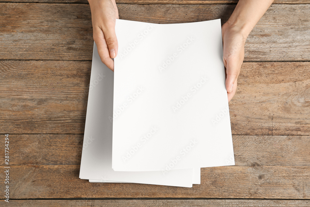 Woman holding blank paper sheets for brochure at wooden table, top view. Mock up Woman holding blank paper sheets for brochure at wooden table, top view. Mock up