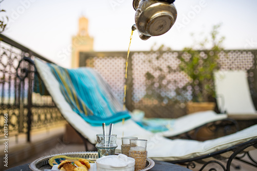 (Selective focus) Moroccan mint tea or Maghrebi mint tea is served by a teapot on the terrace of a Riad in Marrakech, Morocco. Moroccan mint tea is a green tea prepared with spearmint leaves and sugar photo