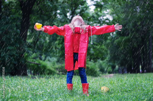 Happy child girl laughs and plays under summer rain