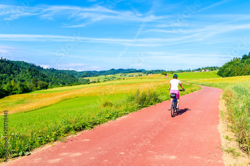 Young woman riding bike on cycling way along green fields near Czorsztynskie lake and Niedzica village  Pieniny Mountains  Poland