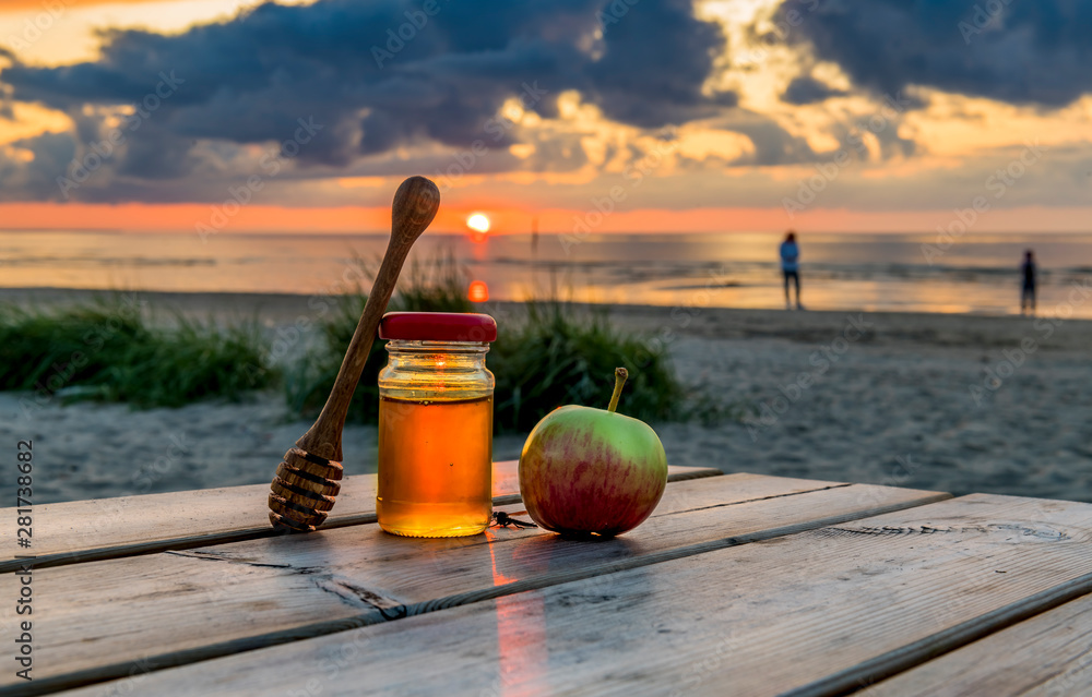 Honey and apples are symbols of Jewish New Year - Rosh ha -Shanah laying on a wooden table, background with blurred defocused sea and colorful sunset