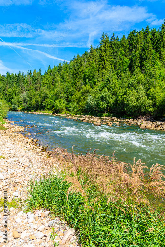 Dunajec river with green hills on shore on sunny summer day near Nowy Targ, Tatra Mountains, Poland