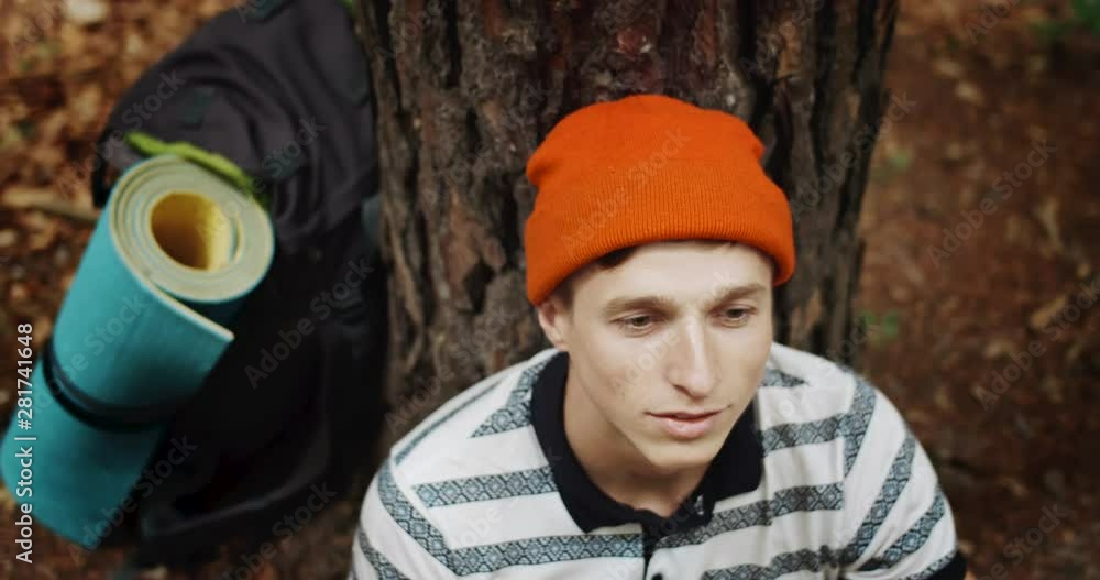 Male hiker in orange hat sitting near tree in forest, looking up and relaxing, active recreation, top view Male hiker in orange hat sitting near tree in forest, looking up and relaxing, active recreation, top view