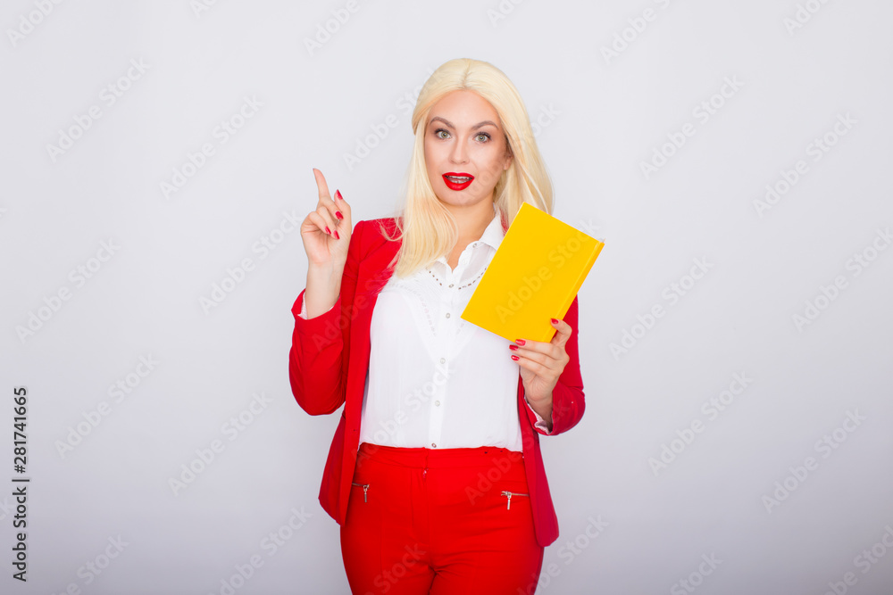 Attractive blonde haired woman wearing red jacket and pants, holding book in her hands Attractive blonde haired woman wearing red jacket and pants, holding book in her hands