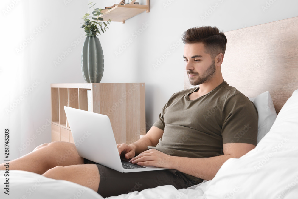Handsome man with laptop resting in bedroom Handsome man with laptop resting in bedroom