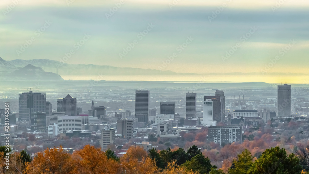 Obraz premium Panorama frame Panorama of populous city with buildings and snowy mountain under cloudy sky