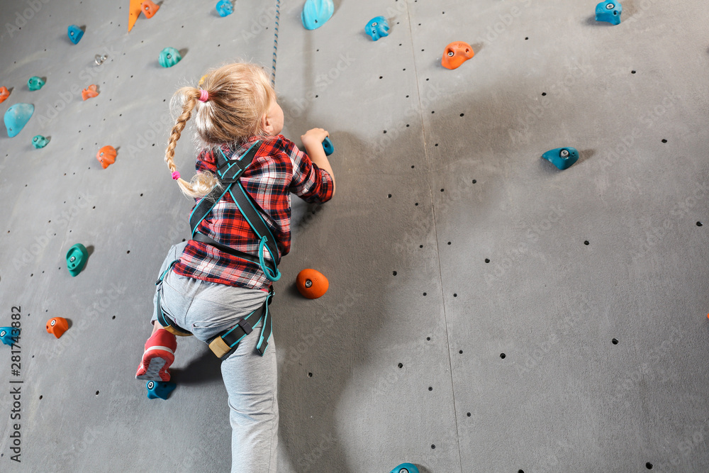Fototapeta premium Little girl climbing wall in gym
