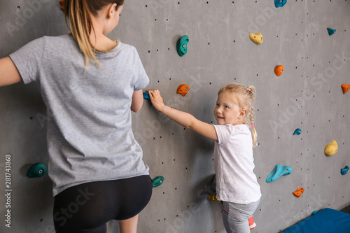 Young woman with her little daughter climbing wall in gym