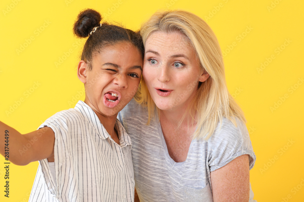 Happy woman with her African-American daughter taking selfie on color background Happy woman with her African-American daughter taking selfie on color background