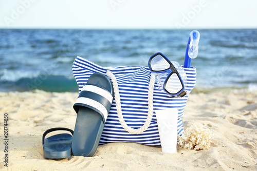 Bag with flip-flops, set or snorkeling and cosmetics on sand beach