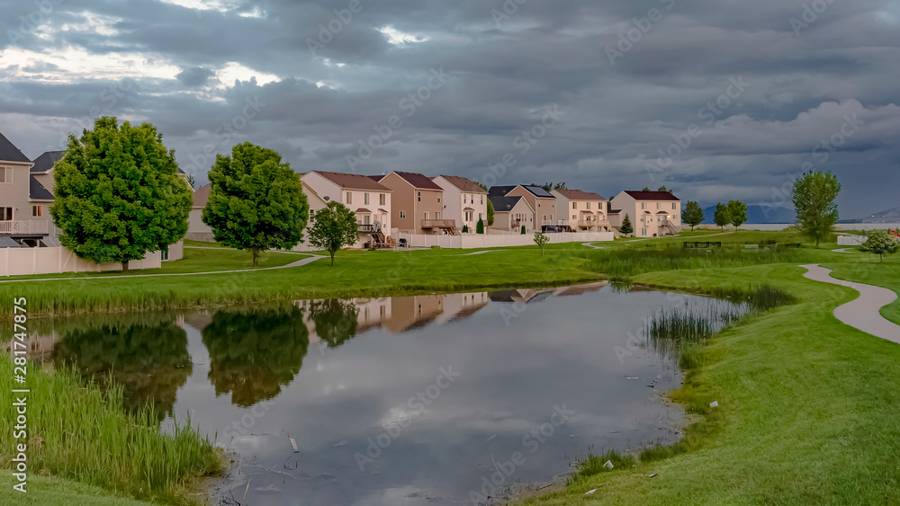 Fototapeta premium Panorama Scenic neighborhood park with a shiny pond and pathway under an overcast sky