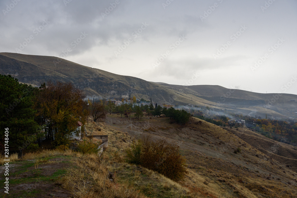 Mountains shrouded in mist in the season of golden autumn on a cloudy day, view of the ancient village in the gorge from the top of the mountain.